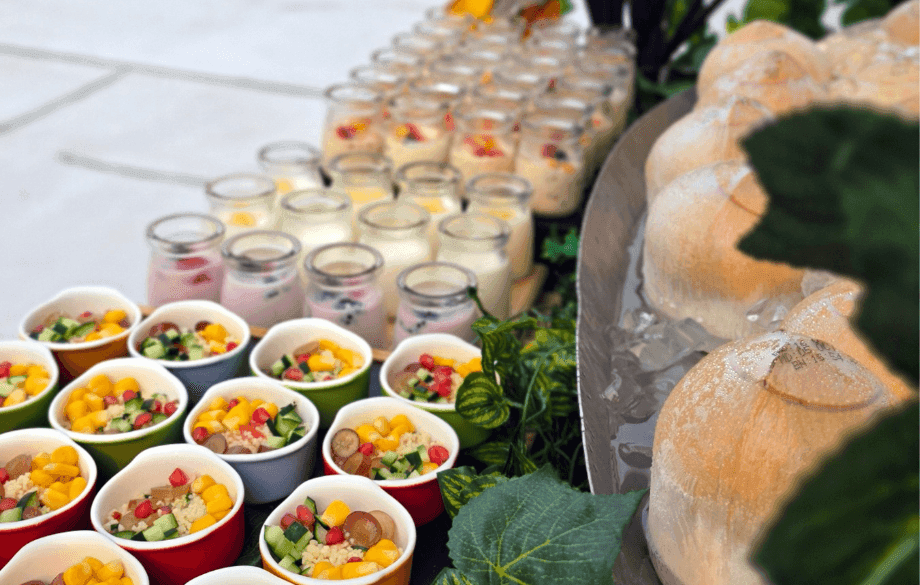 Catering spread with small salads, yogurt parfaits, and whole coconuts on ice.