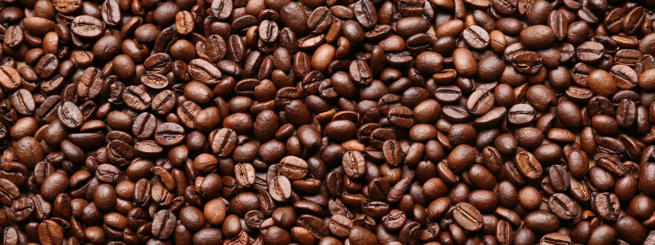 Roasted brown coffee beans scattered densely, showing varied textures and shapes.