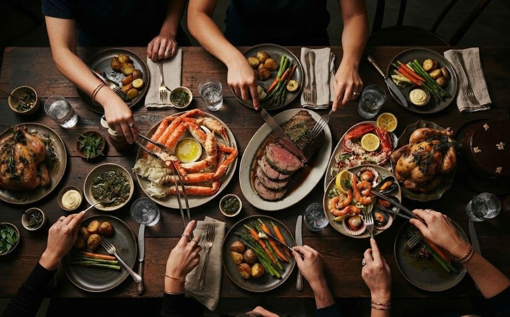 A top-down view of people sharing a large, festive dinner with various dishes.