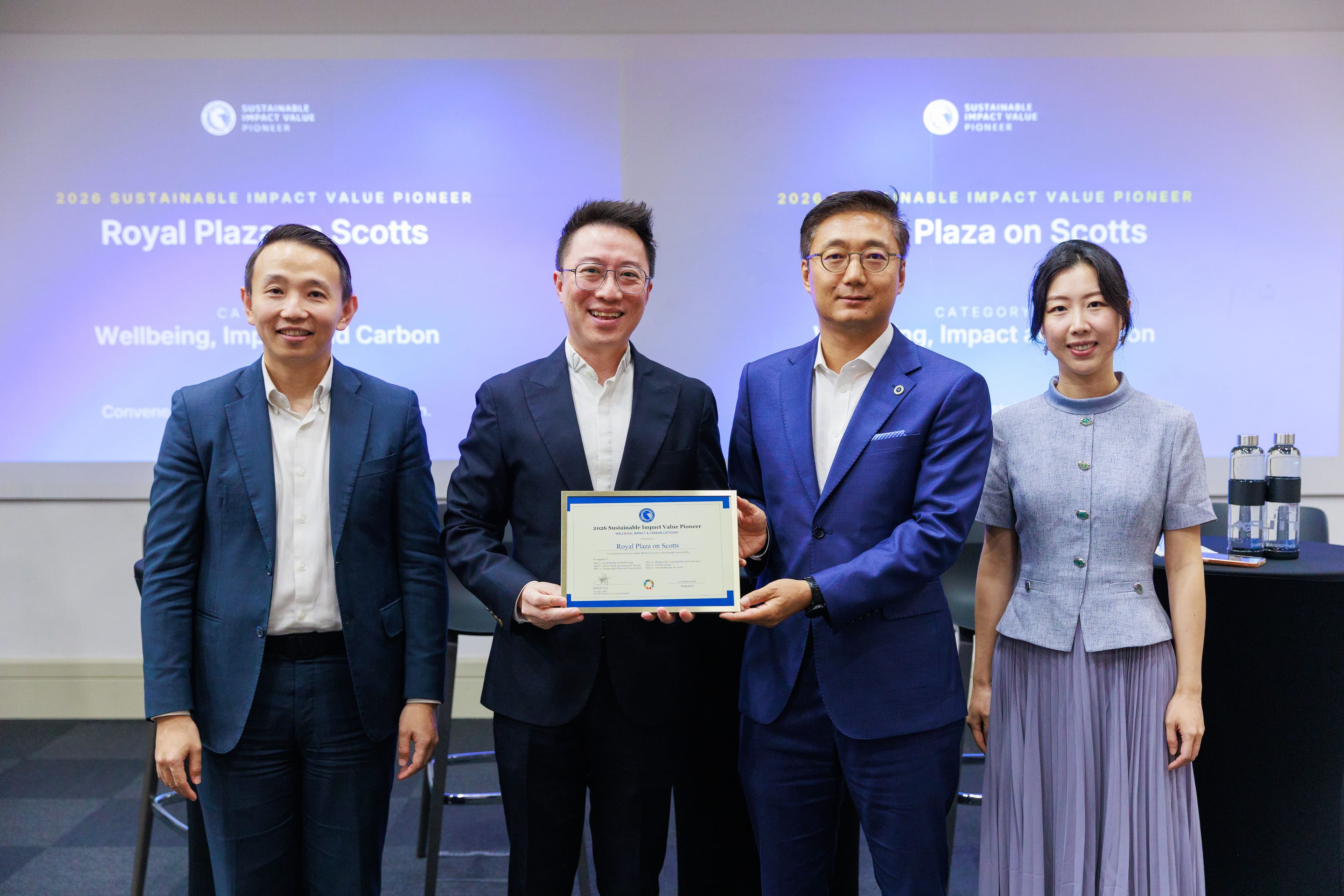 Four professionals at an award ceremony, two men exchanging a certificate.