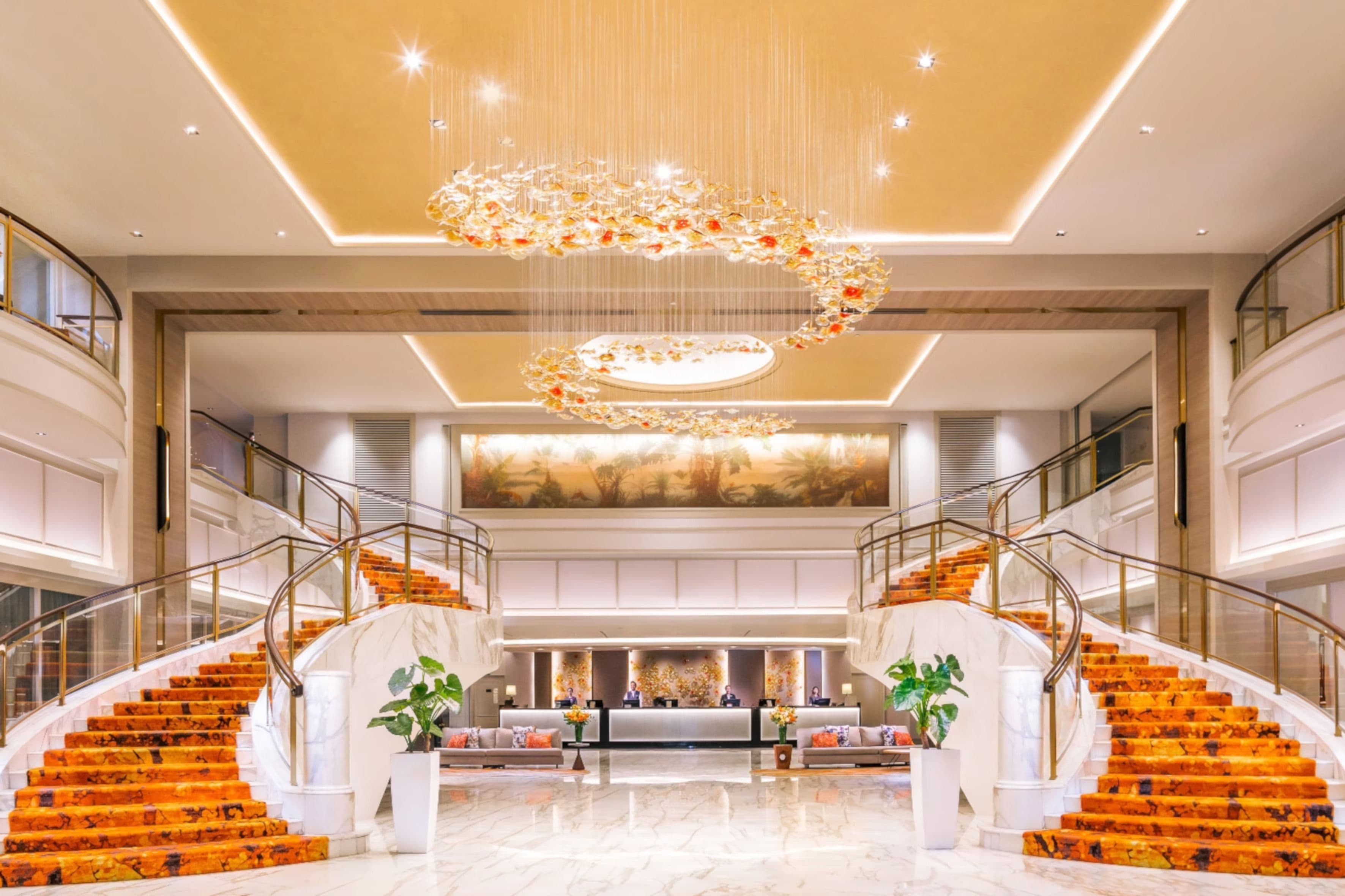 Grand hotel lobby with dual orange carpeted staircases and a modern chandelier.